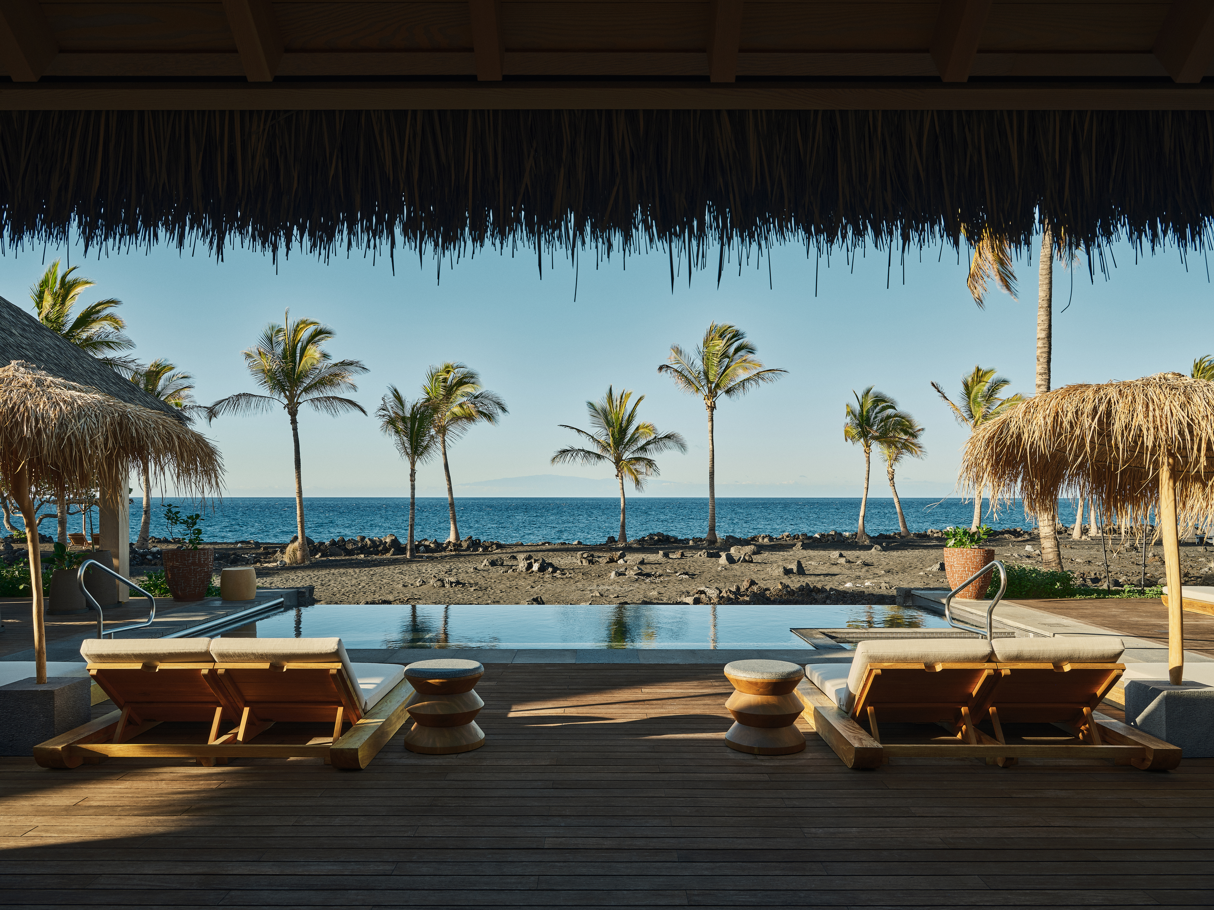 Oceanfront deck with lounge chairs, palm trees, and stunning water view.